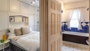 A bedroom with a bed, bedside table, and a bathroom with a bathtub and window.
