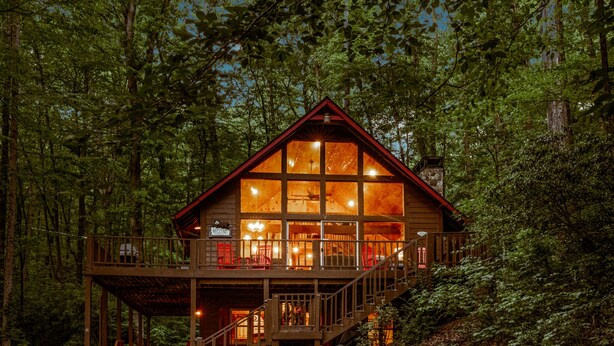 Eine Holzhütte mit Balkon, großen Fenstern und einem Kamin aus Stein.