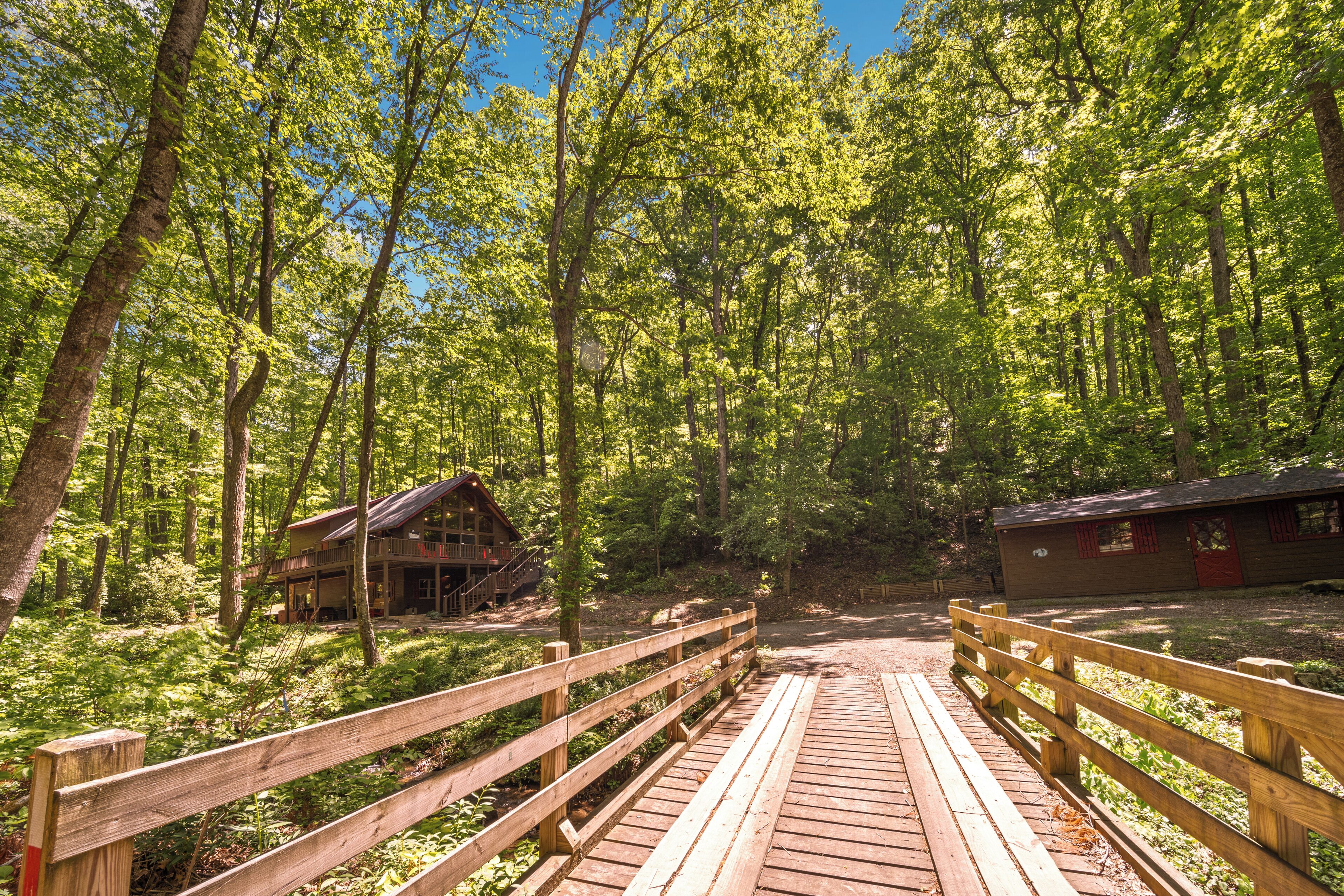 Eine Holzbrücke führt zu einer Hütte in einem bewaldeten Gebiet.