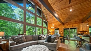 Ein gemütliches Blockhaus-Interieur mit einem großen Ecksofa, einem kuscheligen Hocker und einem Essbereich.