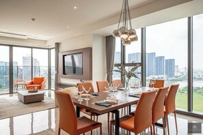 Un espace de repas moderne, avec une grande table dressée pour six personnes, un téléviseur fixé au mur et une vue sur le paysage urbain grâce à de grandes fenêtres.