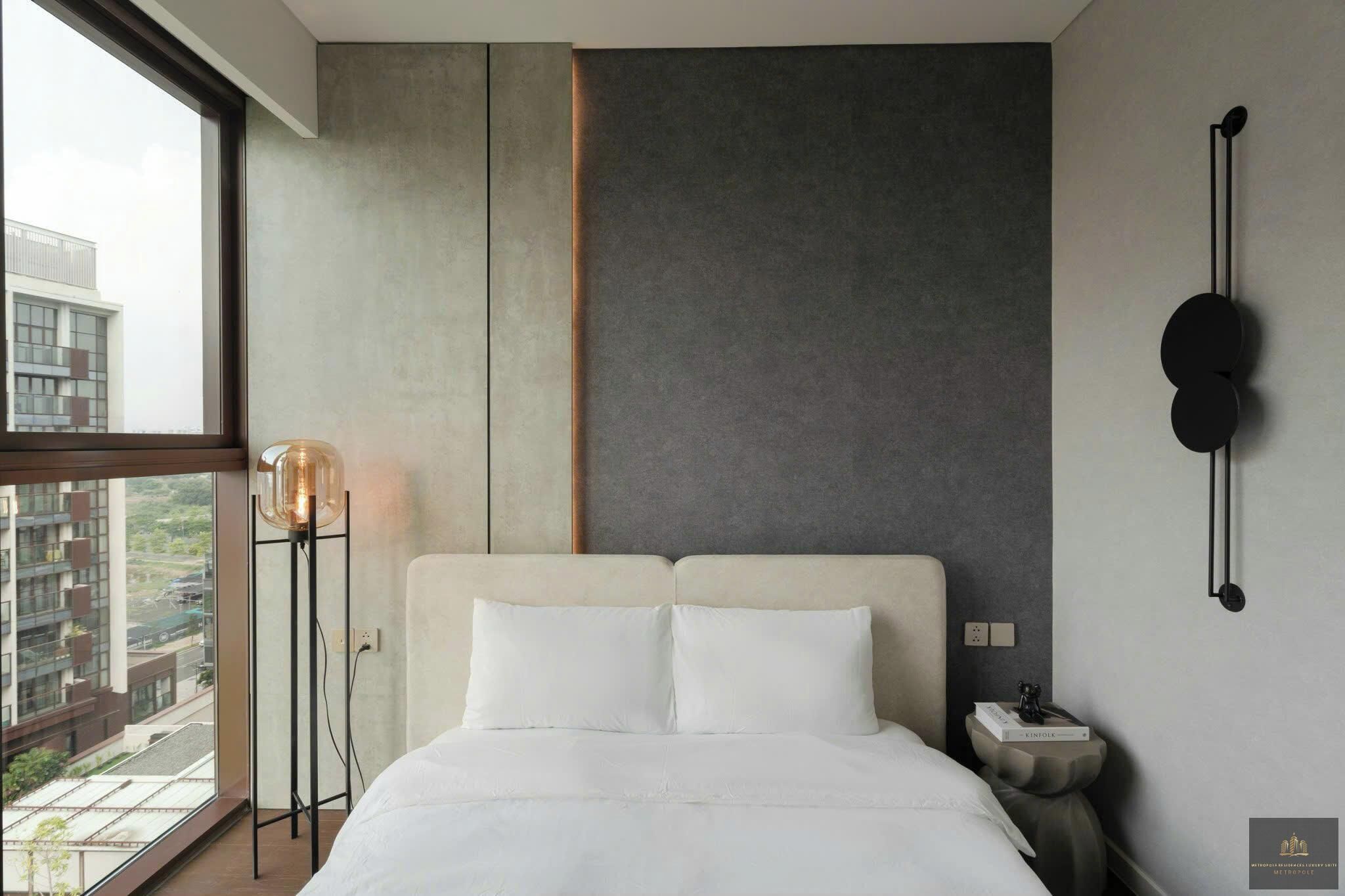 Een moderne hotelkamer met een groot bed, een bedlampje, een wandlamp en uitzicht op de stad door een groot raam.
