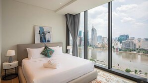 A modern hotel room with a large bed, a city view, and a river. - Metropole Residences Luxury Suite (Ho Chi Minh City)