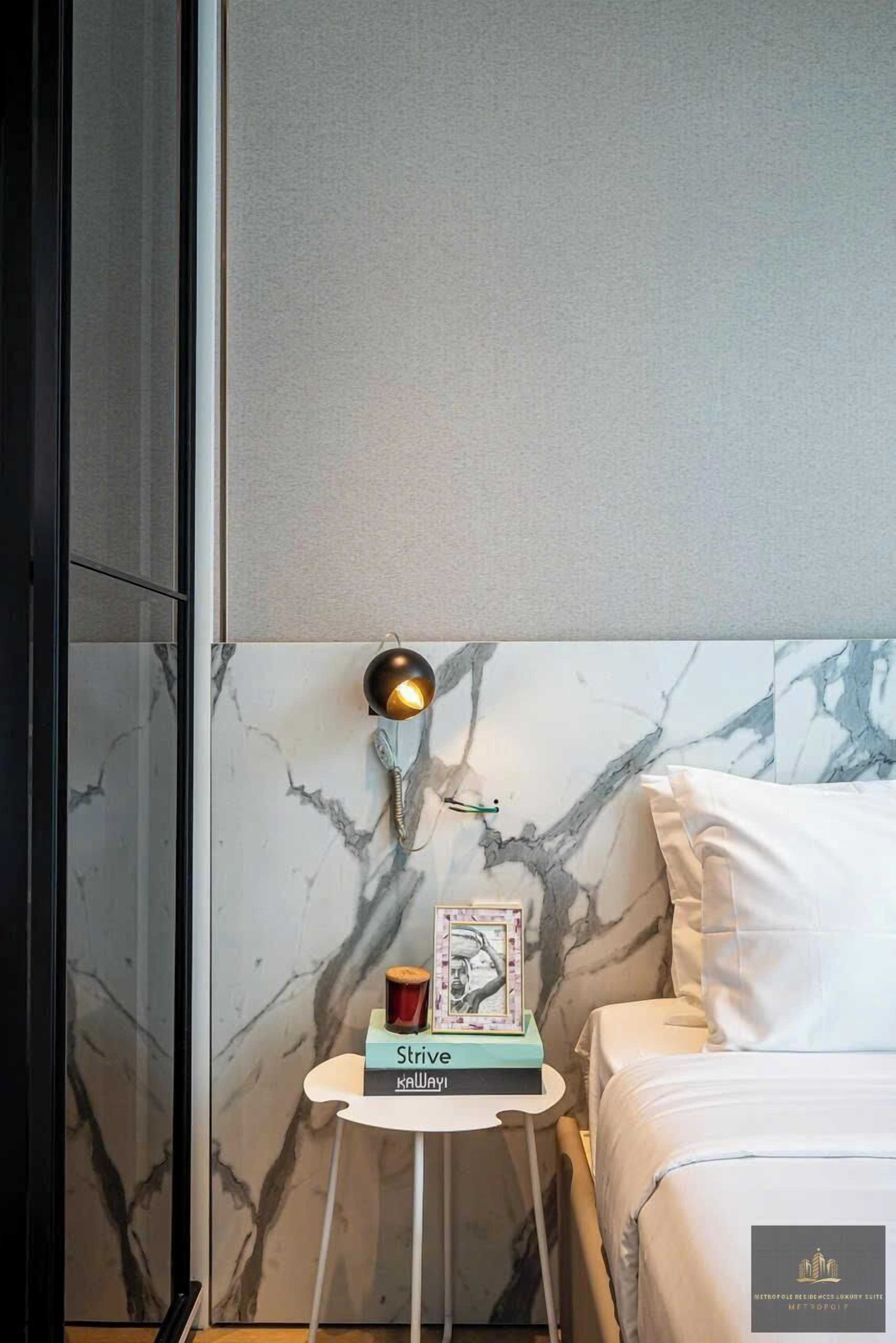 A hotel room with a marble headboard, a bedside table with a lamp, a framed picture, and a small book titled "Strive."