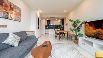 Een moderne woonkamer met een grijze bank, een houten salontafel, en een eethoek met een tafel en stoelen.