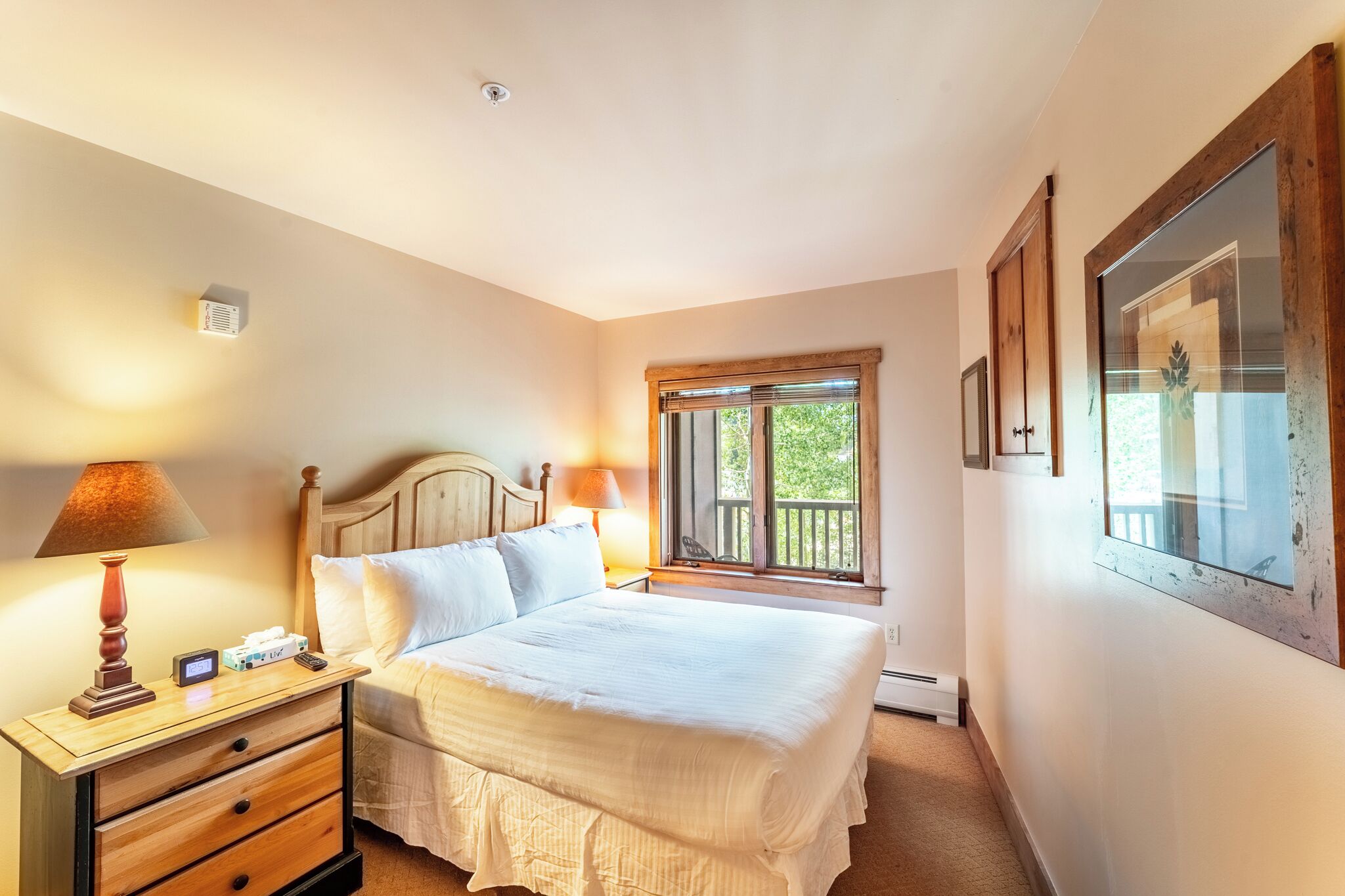 A bedroom with a bed, bedside lamps, a nightstand, a window with a view, and a thermostat.
