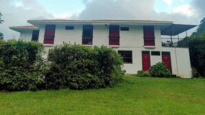 A two-story building with a flat roof, multiple windows with red curtains, and a covered balcony area.