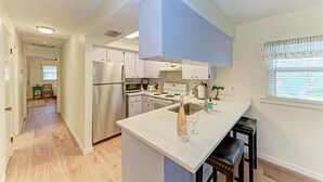 A modern kitchen with white cabinets, stainless steel appliances, and a large island with bar stools. - The Magic Dolphin B, great Holmes Beach location, steps to gulf beaches (Holmes Beach)