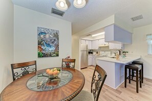 A modern kitchen with white cabinets, stainless steel appliances, and a glass dining table with chairs.