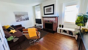 A living room with a sofa, a small table, a fireplace, a television, and a bookshelf. - 🌇DoWnToWn HoUsE🏡 / 3min WALK to TrainSTATION & facilities / Clean-Spacious-Quiet (Harrison)