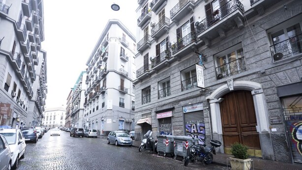 Rua de paralelepípedos ladeada por edifícios altos, carros estacionados e uma motocicleta.