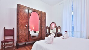 Quarto de hotel com um armário de madeira grande, uma cama com roupa de cama branca, uma cadeira de madeira e um espelho.