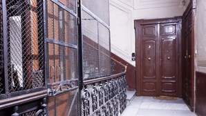 Corrimão de metal com design em tela, porta de madeira e piso de mármore.