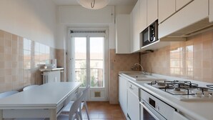 A compact kitchen with a dining table and chairs, a microwave, stove, and oven. - GuestHost - Comfortable 100sqm flat located on the fourth floor (with lift), equipped with kitchen, living area, two bathrooms and two bedrooms that can accommodate up to 4 people. A short walk from Lambrate and Udine stations, it is conveniently located (Milano)