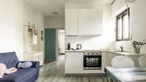 A compact kitchen with a built-in oven, a dining area with a table, and a sofa. - GuestHost - Pineta di Ponente Apartment (Viareggio)