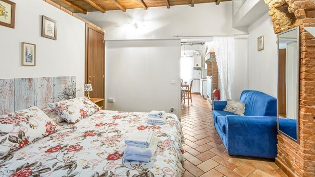 Quarto com cama, sofá azul, teto de madeira e parede de tijolos.