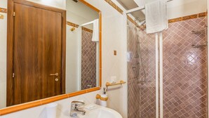 Casa de banho com porta de madeira, pia, espelho e zona de duche com parede em azulejos.