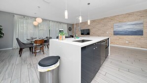 Eine moderne Küche mit Kochinsel, ein Essbereich mit Tisch und Stühlen sowie ein Wohnbereich mit Fernseher und Kunstwerken an der Wand.
