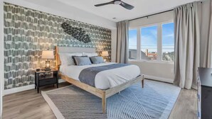 Een moderne slaapkamer met een groot bed, een plafondventilator, een nachtkastje met een lamp, een raam met gordijnen en uitzicht op de stad.