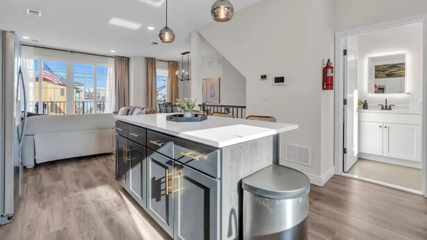 Een moderne keuken met een centraal kookeiland, hanglampen en uitzicht op buiten.