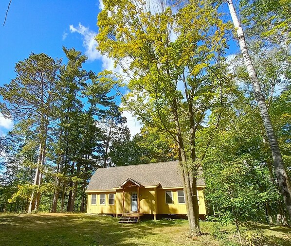 A yellow house with a porch, surrounded by trees and a clear blue sky.