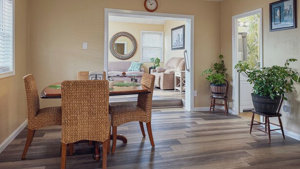 A dining area with a wooden table and wicker chairs, a sofa, and a potted plant. - Relaxing 2BR/2BA Entire House, Short Drive from Wildwood & Cape May Beaches (Middle Township)