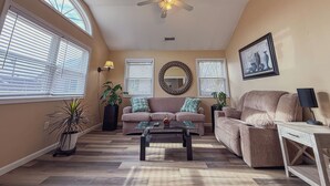 A spacious living room with a ceiling fan, large windows, a sofa, a coffee table, and a side table with a lamp. - Relaxing 2BR/2BA Entire House, Short Drive from Wildwood & Cape May Beaches (Middle Township)