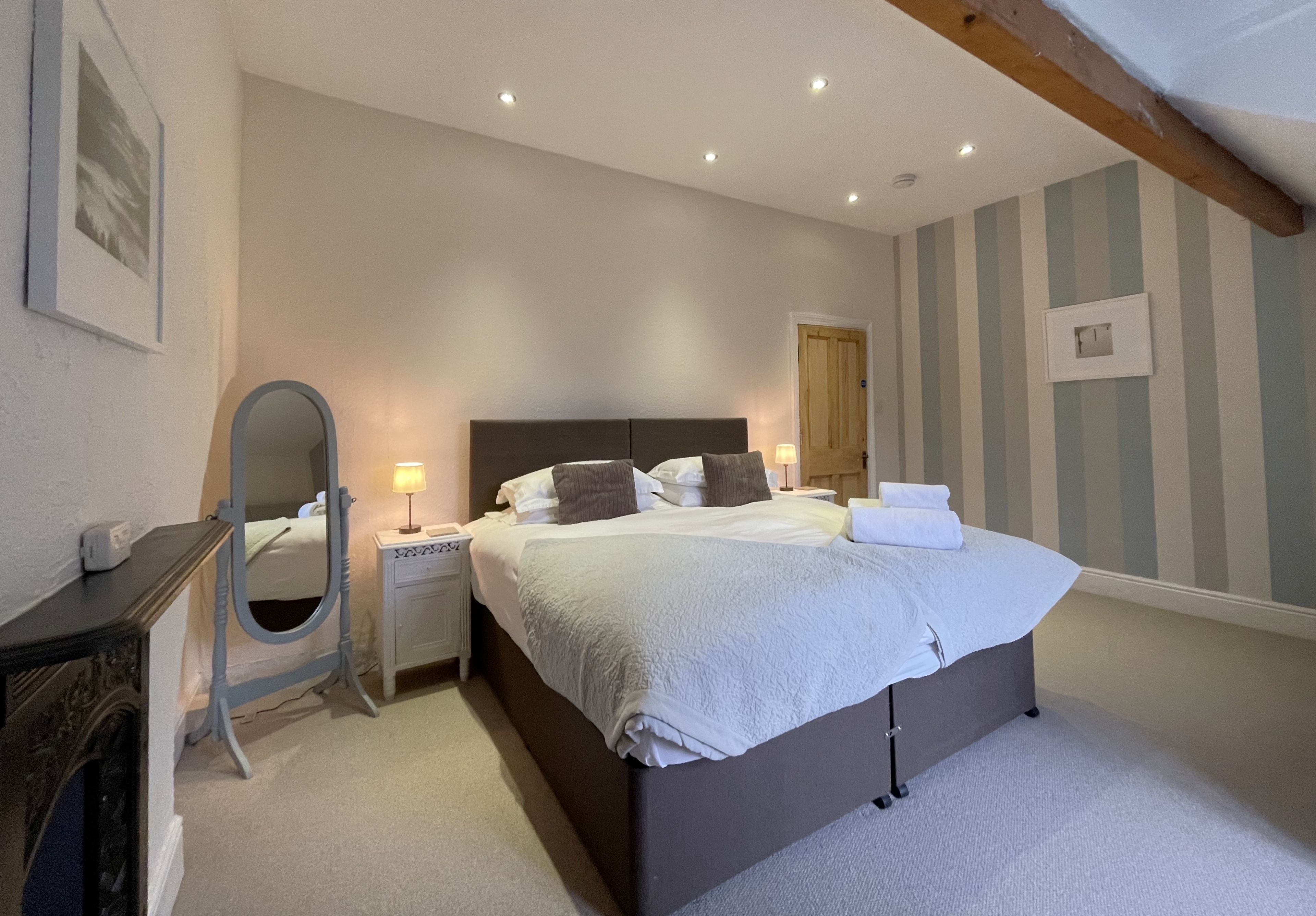 A bedroom with a large bed, bedside lamps, a dresser, a mirror, and a door.