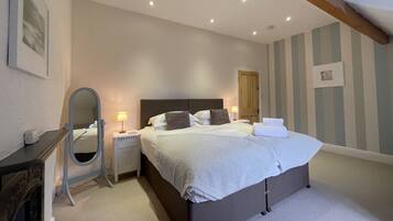 A bedroom with a large bed, bedside lamps, a dresser, a mirror, and a door.