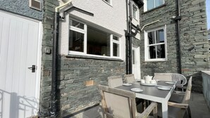 An outdoor patio with a stone wall, a white door, and a table set for dining. - 45 Eskin Street  - sleeps 6 guests  in 3 bedrooms (Central Keswick)