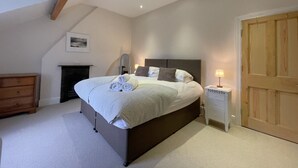 A bedroom with a large bed, a wooden dresser, a nightstand with a lamp, and a door. - 45 Eskin Street  - sleeps 6 guests  in 3 bedrooms (Central Keswick)