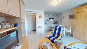 Un espacio habitable compacto con kitchenette, comedor y zona de estar con una silla a rayas.