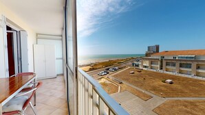 Un balcón con vista a la playa, un comedor con mesa y sillas, y un estacionamiento con varios coches.