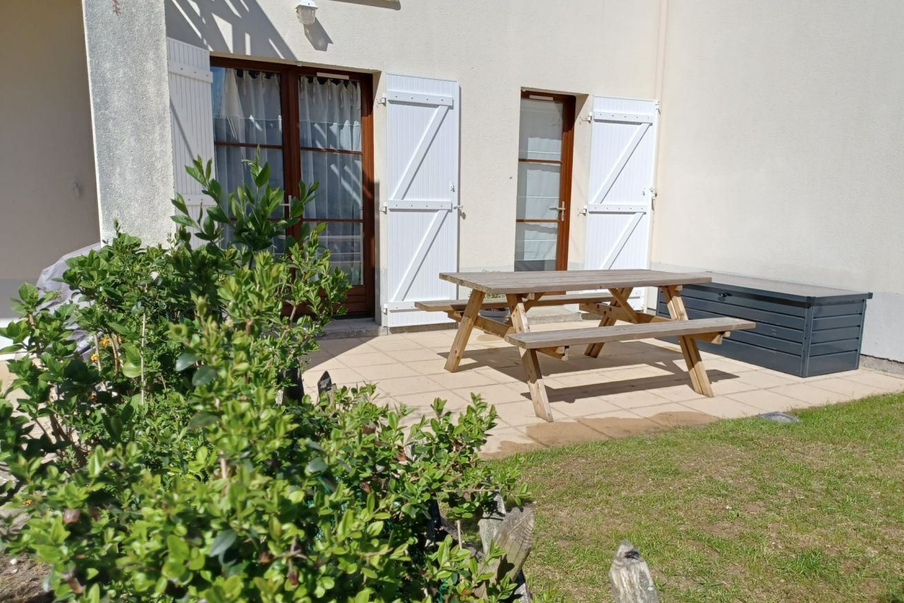 Eine Terrasse mit Holztisch und Bänken, umgeben von Kübelpflanzen und einem kleinen Garten.