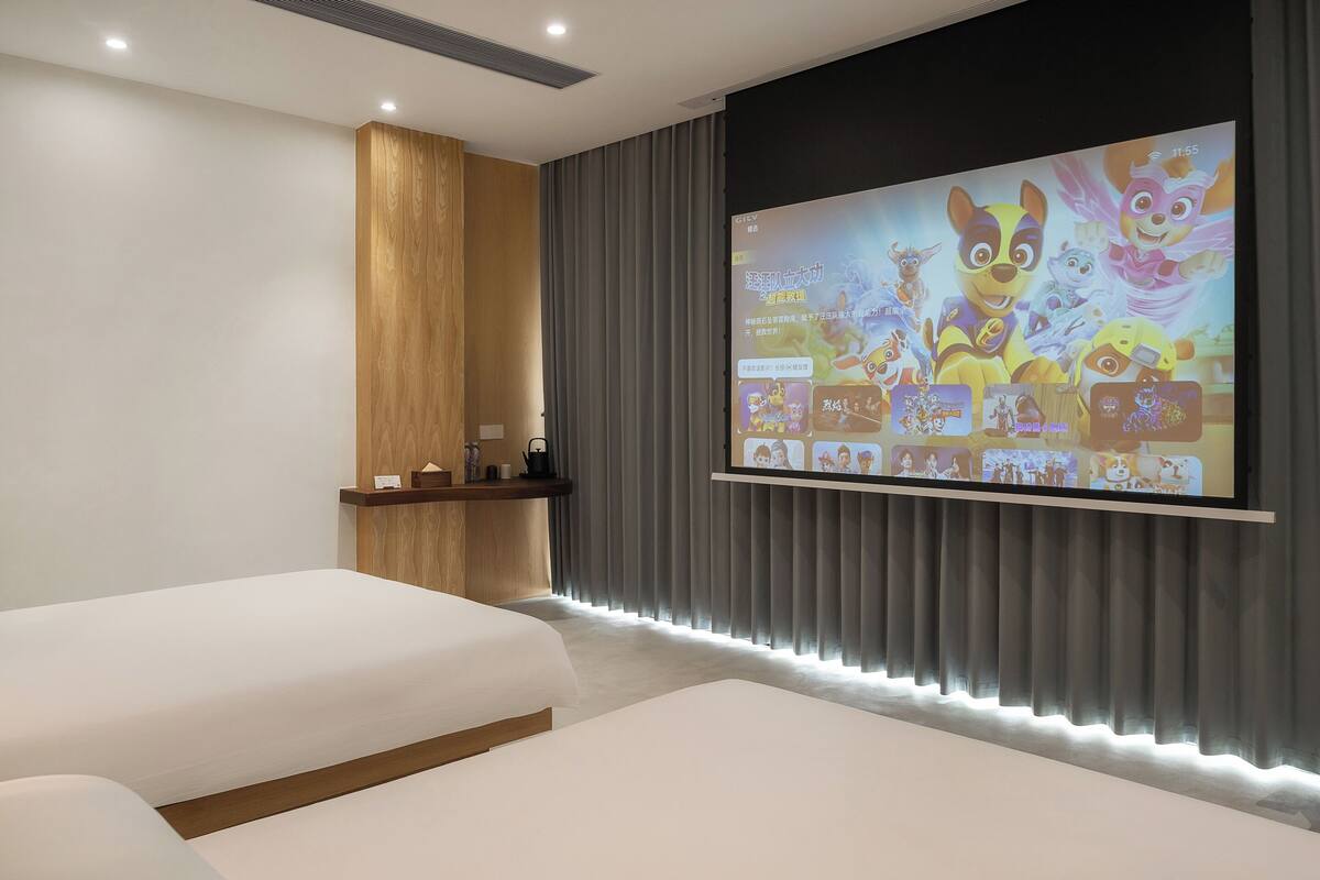 A modern hotel room with a large screen displaying animated characters, a wooden accent wall, and a cozy seating area.