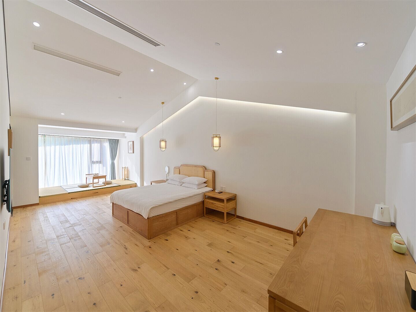 Ein geräumiges Schlafzimmer mit einem großen Bett, Nachttischen, einem Holztisch und einem großen Fenster mit Vorhängen.