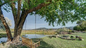 A wooden swing hanging from a large tree over a pond, surrounded by grass and rocks. - Serene River Place Retreat Unit 2, 1-bedroom condo nestled along the river in Howard, CO. (Howard)
