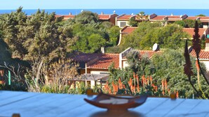 A coastal residential area with terracotta-roofed houses, lush greenery, and a view of the sea.