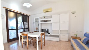 A room with a dining table, chairs, a sofa, a TV, and built-in shelves.
