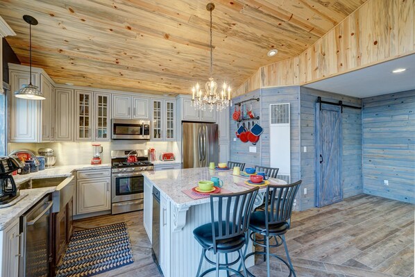A kitchen with wooden ceiling, white cabinets, stainless steel appliances, and a central island with chairs.