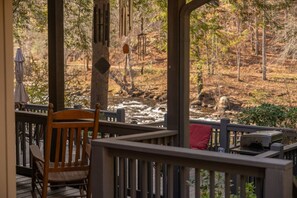 A wooden deck with a chair and a grill, overlooking a forested area with a stream. - River Zen, A Toccoa River Retreat (Blue Ridge)