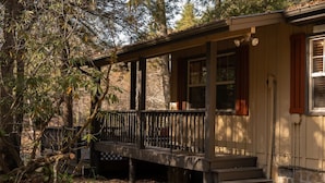 A wooden cabin with a porch, steps leading to the entrance, and a view of the surrounding forest.
