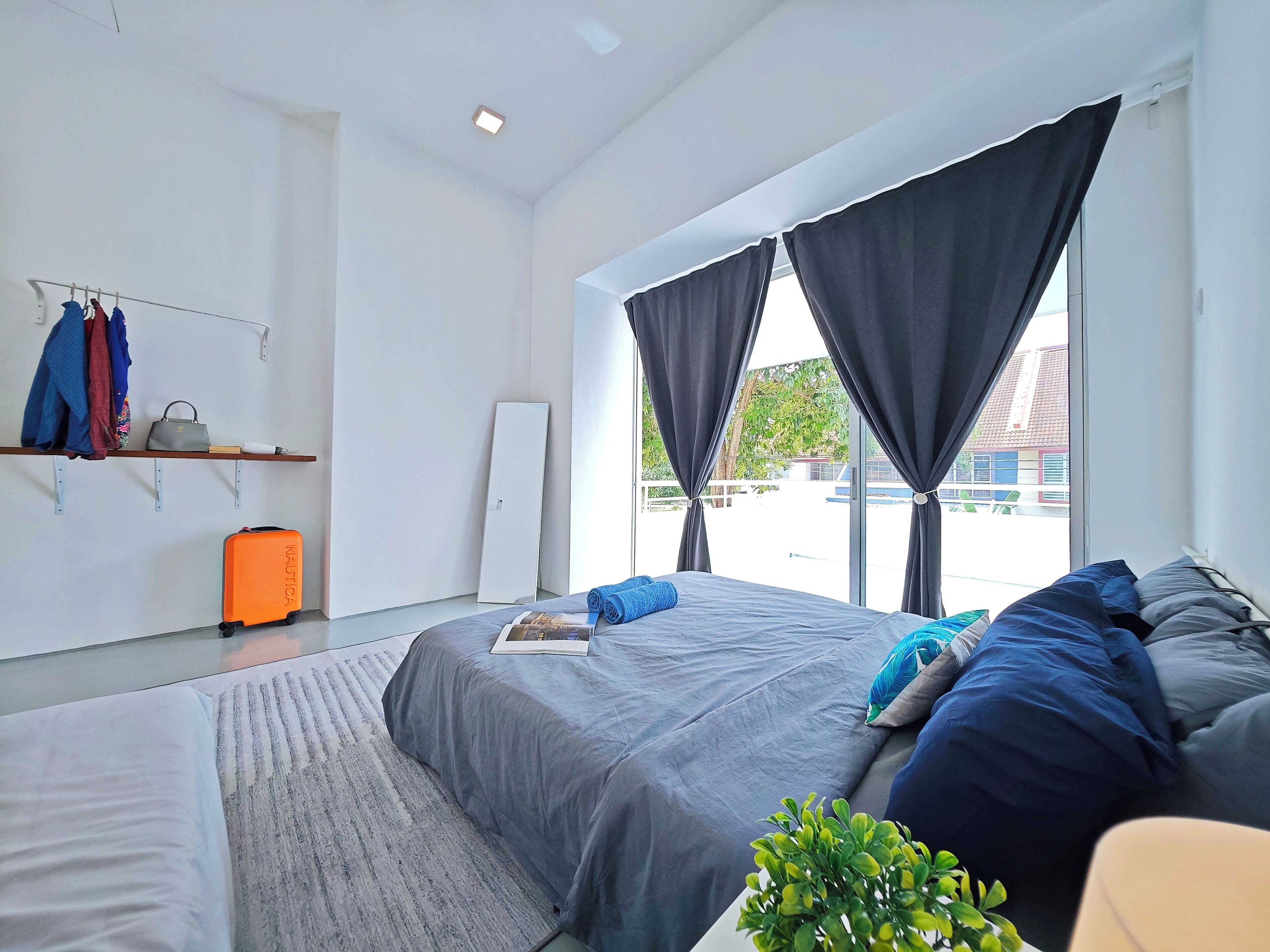 Quarto de hotel moderno com uma cama grande, uma secretária pequena e uma janela com cortinas.