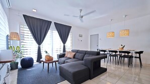 A modern living room with a grey sectional sofa, a dining table with chairs, and a ceiling fan. - Cosy Batu Kawan Homestay 12 pax ~ 5 mins to Design Village & IKEA ~ Entire Home (Simpang Ampat)