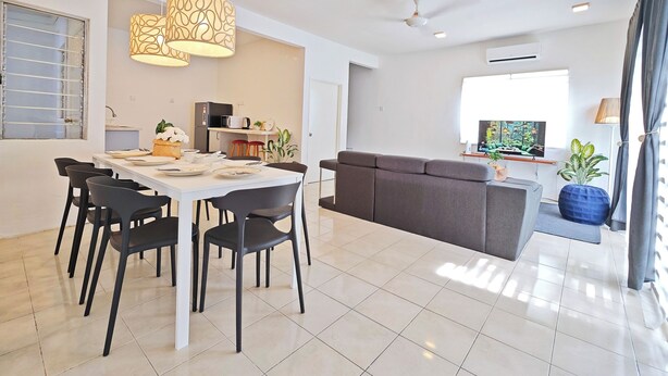 A modern living room with a grey sofa, a dining area with a white table and black chairs, and a kitchen area with a microwave and refrigerator. - Cosy Batu Kawan Homestay 12 pax ~ 5 mins to Design Village & IKEA ~ Entire Home (Simpang Ampat)