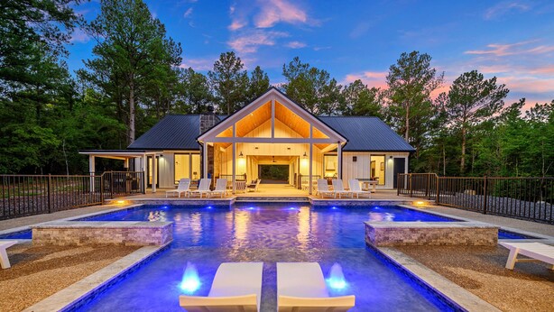 Una casa moderna con piscina, sillas de descanso y un patio cubierto.
