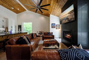 Rustic modern living room with cozy leather sofas, fireplace, and open kitchen.