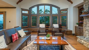 A spacious living room with a large arched window, leather sofas, a wooden coffee table, and a stone fireplace.