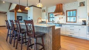 A modern kitchen with a central island, wooden bar stools, and pendant lighting.