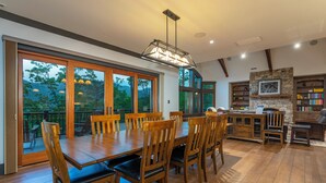 A spacious dining area with a large wooden table and chairs, a hanging light fixture, and a stone fireplace.
